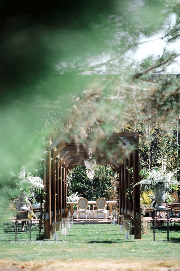 O espaço da cerimónia no jardim do Aqueduto: pérgula de madeira com candelabro, cadeiras e flores brancas